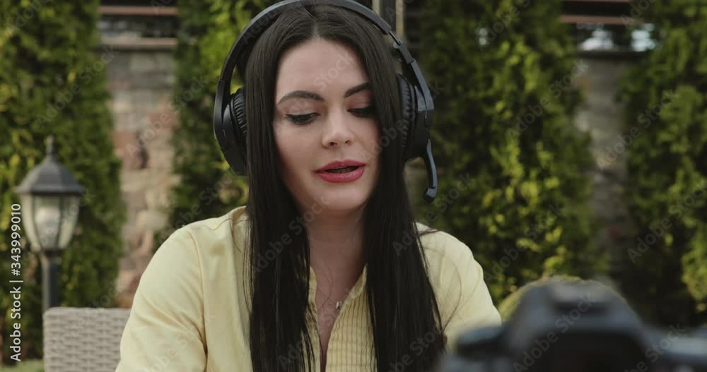 Pretty blogger talking on the radio microphone to the camera in windy garden