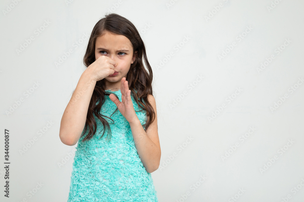 teen girl in a blue dress covered her nose with her hands on a white studio background teen girl in a blue dress covered her nose with her hands on a white studio background
