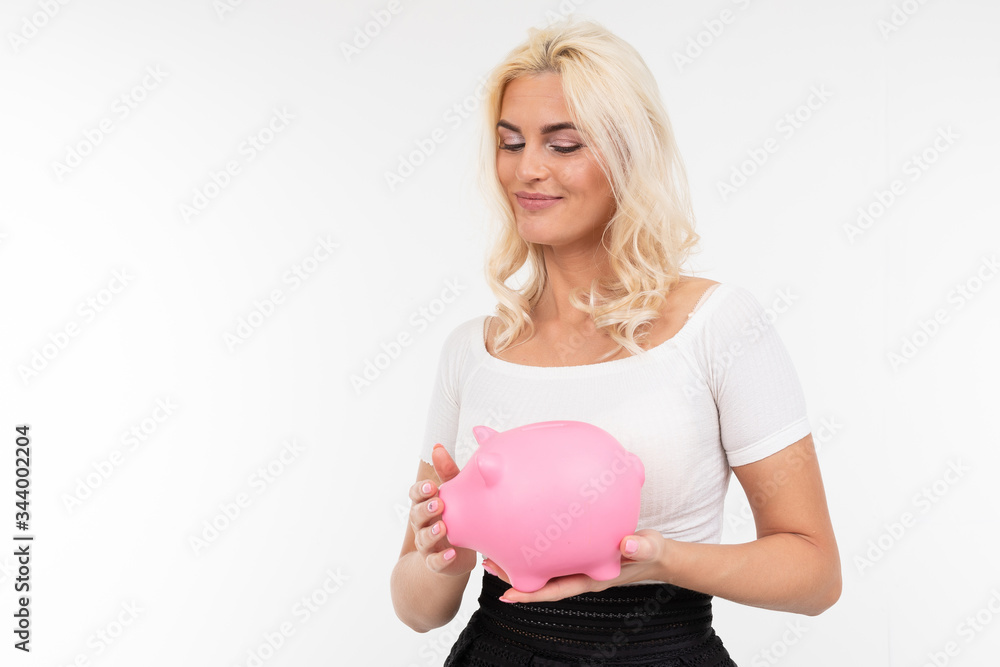 charming blonde woman in a white t-shirt holds a piggy bank on a white background with copy space charming blonde woman in a white t-shirt holds a piggy bank on a white background with copy space
