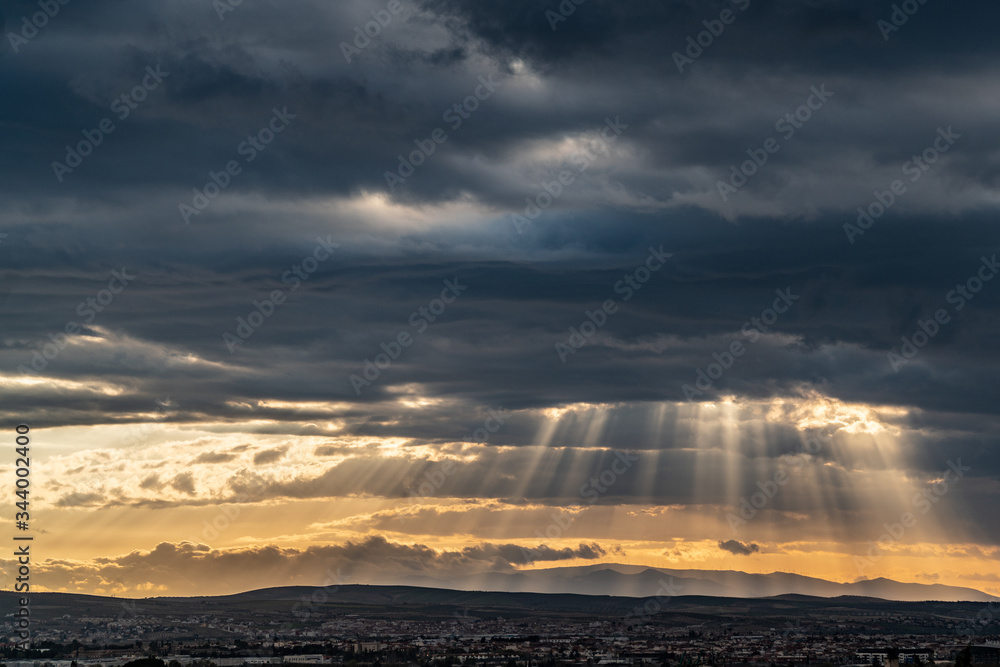 Panoramic view of dramatic sun ray through low clouds over city at sunset. The sun cuts through the clouds over the city. Sunbeams on the city