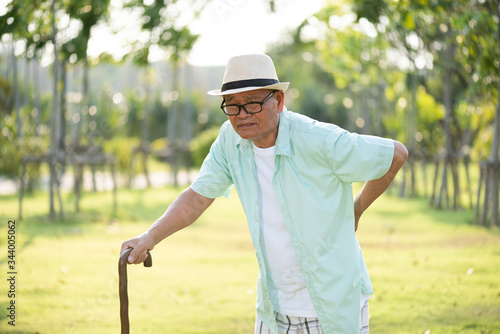 Asian old man walking in park and having a back pain, backache. Senior healthcare concept.