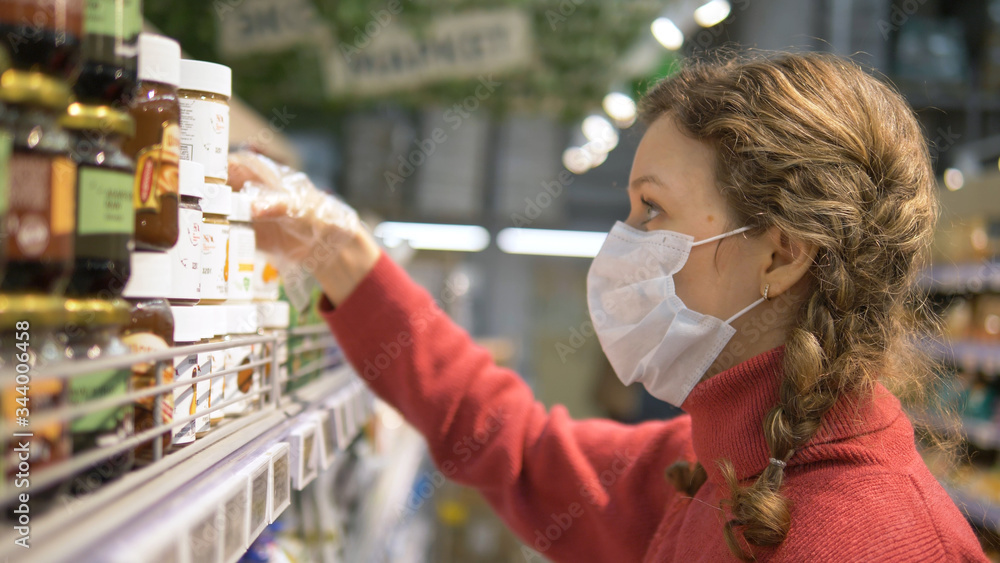 portrait of beautiful young girl in medical mask and disposable gloves reads label on products in supermarket, studies composition of product, personal protection coronavirus portrait of beautiful young girl in medical mask and disposable gloves reads label on products in supermarket, studies composition of product, personal protection coronavirus