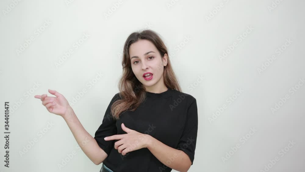 Cute young brunette woman in black t-shirt, blue jeans with belt on gray background, smiling happy girl shows her fingers in the direction of the side Cute young brunette woman in black t-shirt, blue jeans with belt on gray background, smiling happy girl shows her fingers in the direction of the side