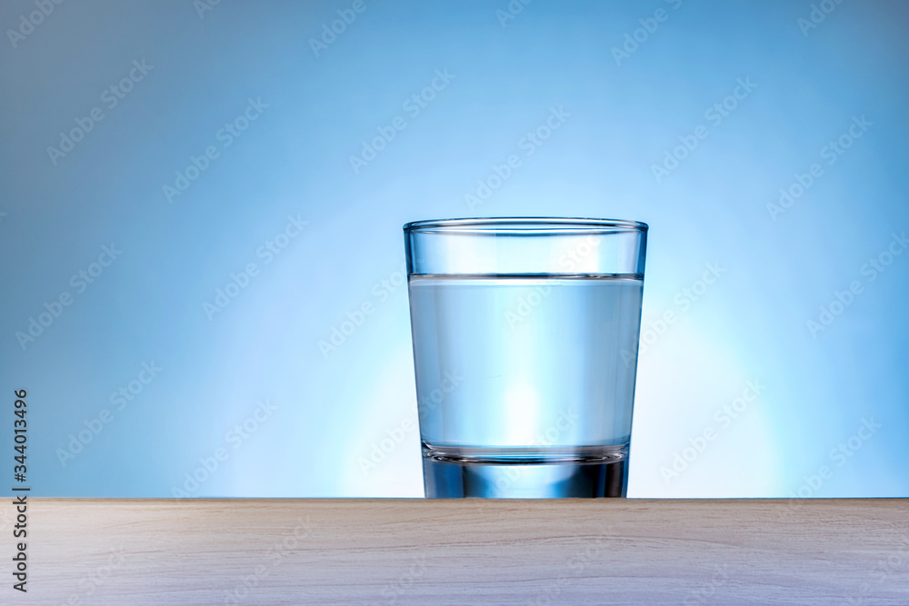 Drinking water against blue background. Glass of pure water on wooden table with copy space. Drinking water against blue background. Glass of pure water on wooden table with copy space.