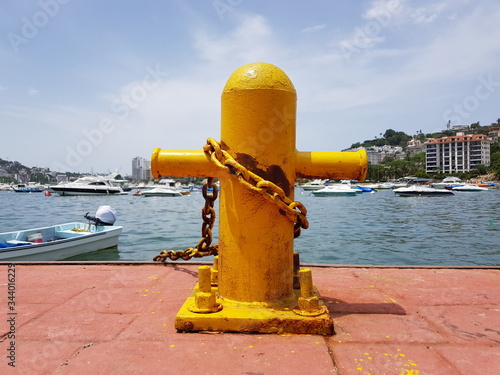 Yellow cruciform steel bitts with the sea in the background on the Acapulco boardwalk