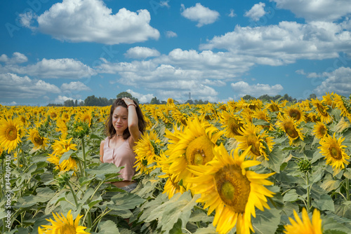 Young teen girl standing in field surrounded by sunflowers and running her hand through her hair