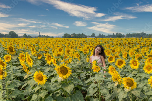 Young teen girl standing in field surrounded by sunflowers
