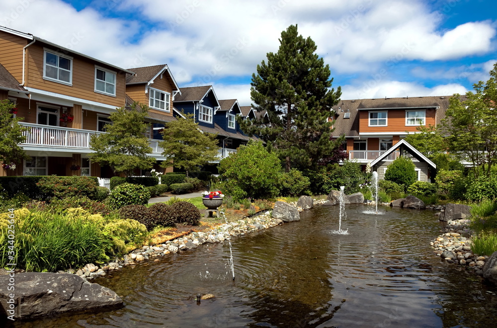 Residential District in Richmond City, a village of townhouses with pond and fountain, green grass bushes and trees in the territory of residential complex, cloudy sky, Vancouver, British Columbia  