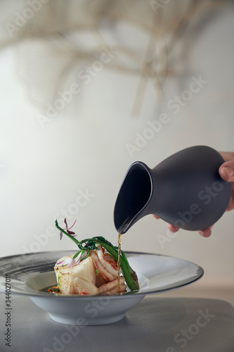 hand pouring broth over poached fish and shrimp