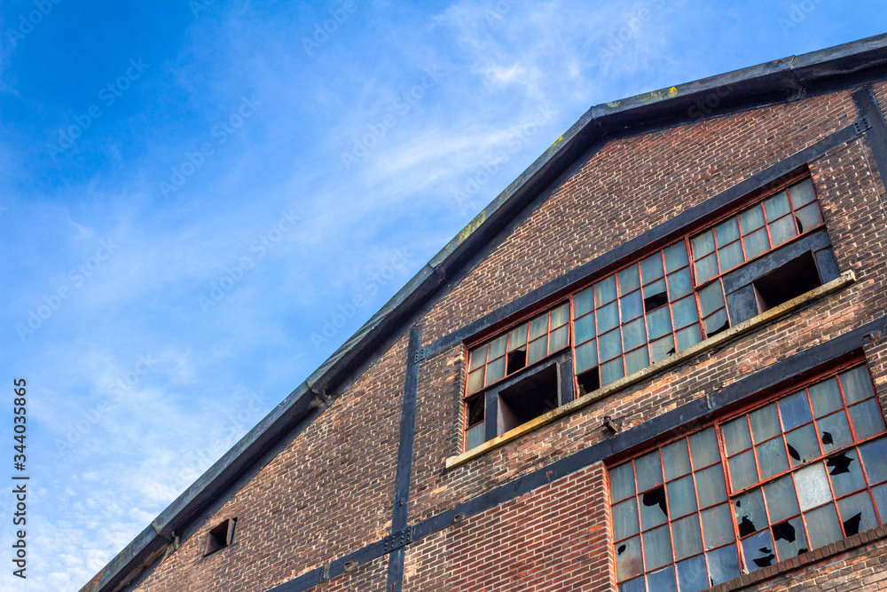 Abandoned warehouse building, brick facade with broken windows, blue sky copy space, horizontal aspect