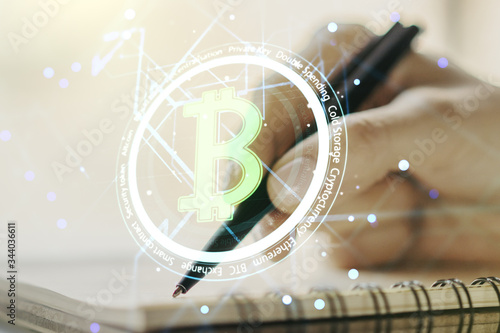 Double exposure of creative Bitcoin symbol hologram with woman hand writing in notepad on background. Mining and blockchain concept © Pixels Hunter