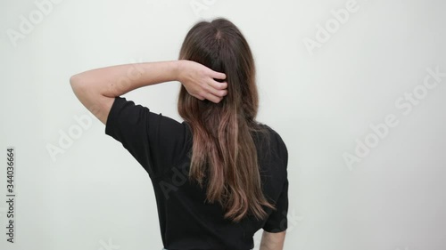 Cute young brunette woman in black t-shirt on gray background, the girl turned her back to camera and holds her hand in long hair