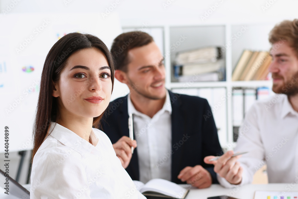Beautiful smiling cheerful girl at workplace look in camera with colleagues group in background. White collar worker at workspace job offer modern lifestyle client visit profession train concept Beautiful smiling cheerful girl at workplace look in camera with colleagues group in background. White collar worker at workspace job offer modern lifestyle client visit profession train concept