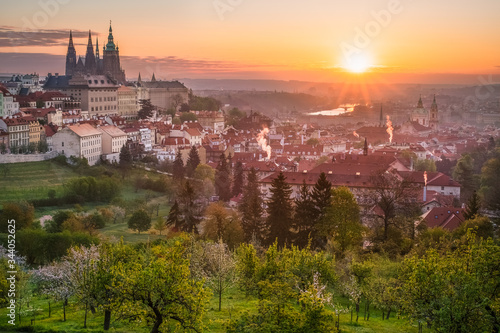 Prague Castle  St. Vitus cathedral and the UNESCO heritage site of the old city center with red rooftops captured behind blooming apple orchard from Strahov monastery during sunrise  Czech Republic