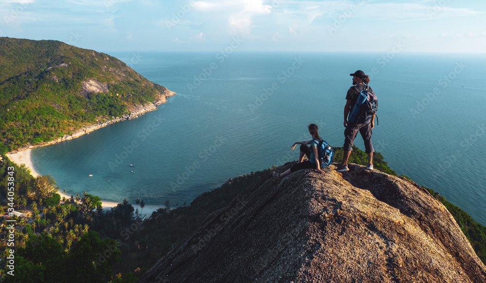 Man and woman stand on on top of cliff at tropical island , enjoying view of nature