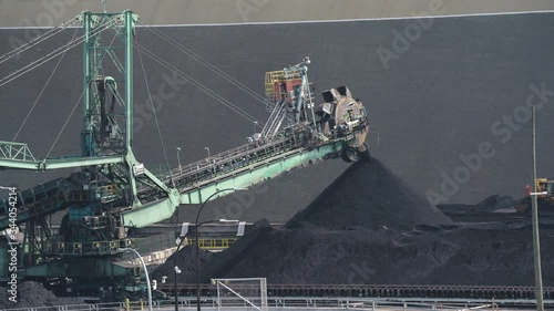 A time lapse of a large stacker machine piling coal in North Vancouver port while tiny-looking bulldozer flattens out piles  photo