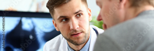 Portrait of serious doc indicating diagnosis to man. Physician wearing white uniform and stethoscope. Medical treatment and health care concept. Blurred background