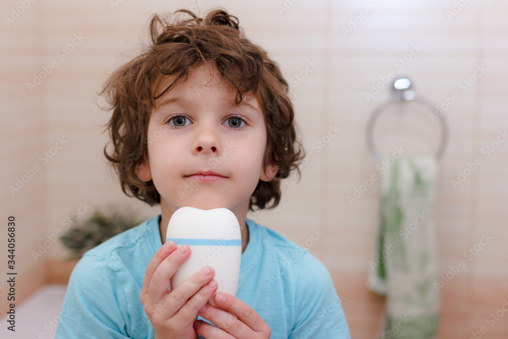 cute curly boy holds big tooth in bathroom. The concept of children's health, medicine. cute curly boy holds big tooth in bathroom. The concept of children's health, medicine.