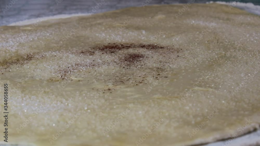 Sprinkle the rolled yeast dough with cinnamon for baking buns. Selective focus. Sprinkle the rolled yeast dough with cinnamon for baking buns. Selective focus.
