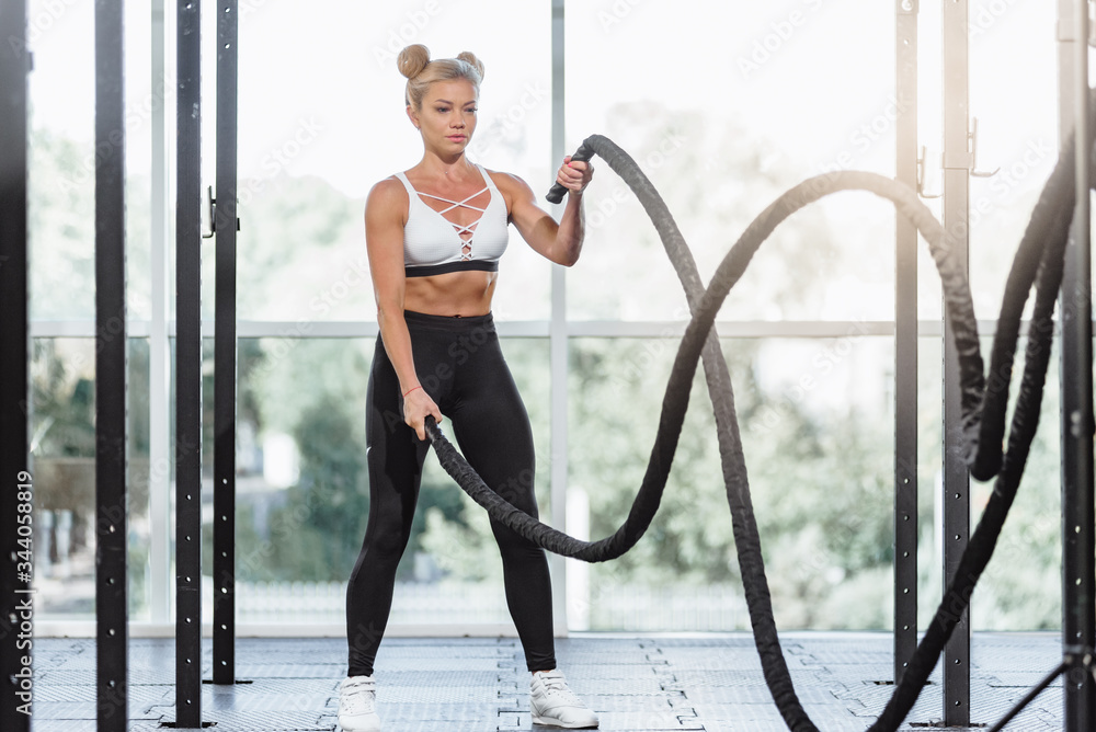 Fit athletic young woman doing functional training with battle rope
