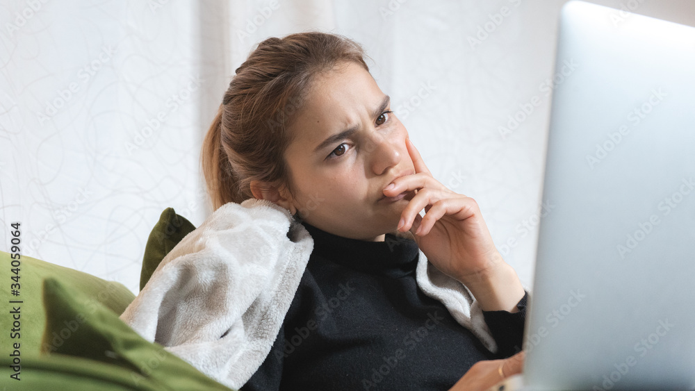 Focused and concerned young girl using a computer at home. Stressed woman working from her couch. Focused and concerned young girl using a computer at home. Stressed woman working from her couch.