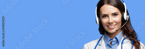 Medical call center servise. Online helping and consultation. Portrait of female doctor in headset, against blue color background, with copy space empty place for some sign text or slogan.