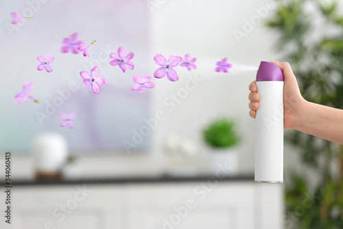 Woman spraying floral air freshener at home