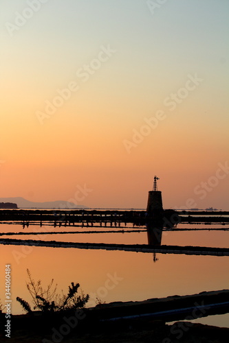 salt pans with water pumping tower and promontory in the background at sunset