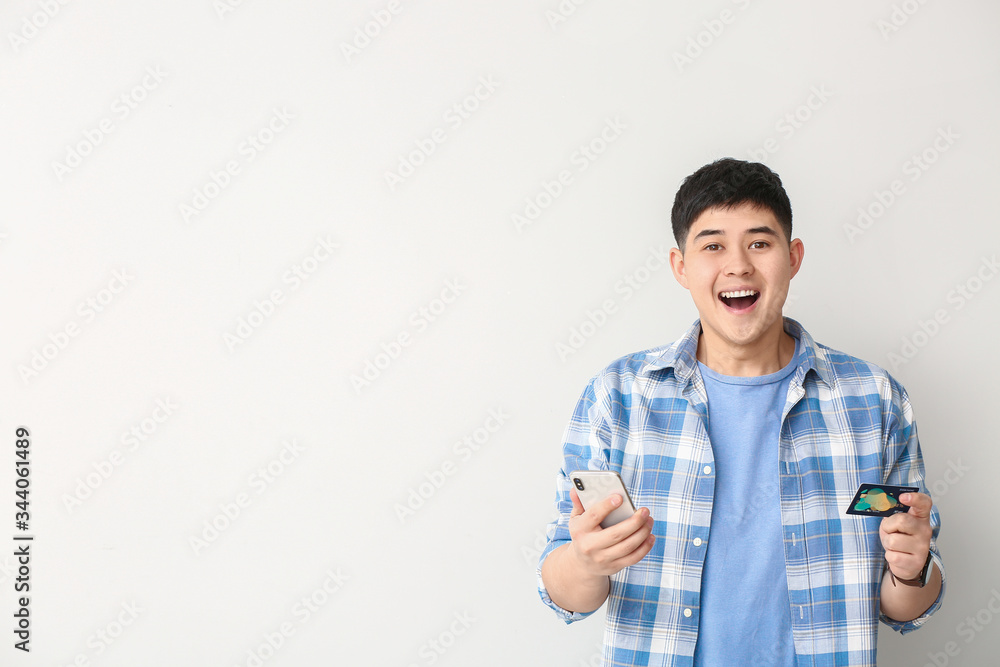 Happy Asian man with credit card and mobile phone on white background Happy Asian man with credit card and mobile phone on white background