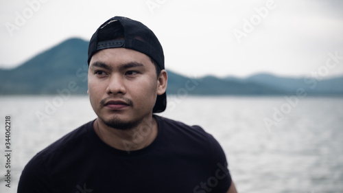 Portrait of Young asian man wearing hat sitting relaxing near riverside blurred nature background