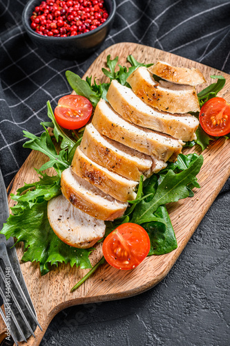 Fresh salad with grilled chicken breast, arugula and tomato. Black background. Top view