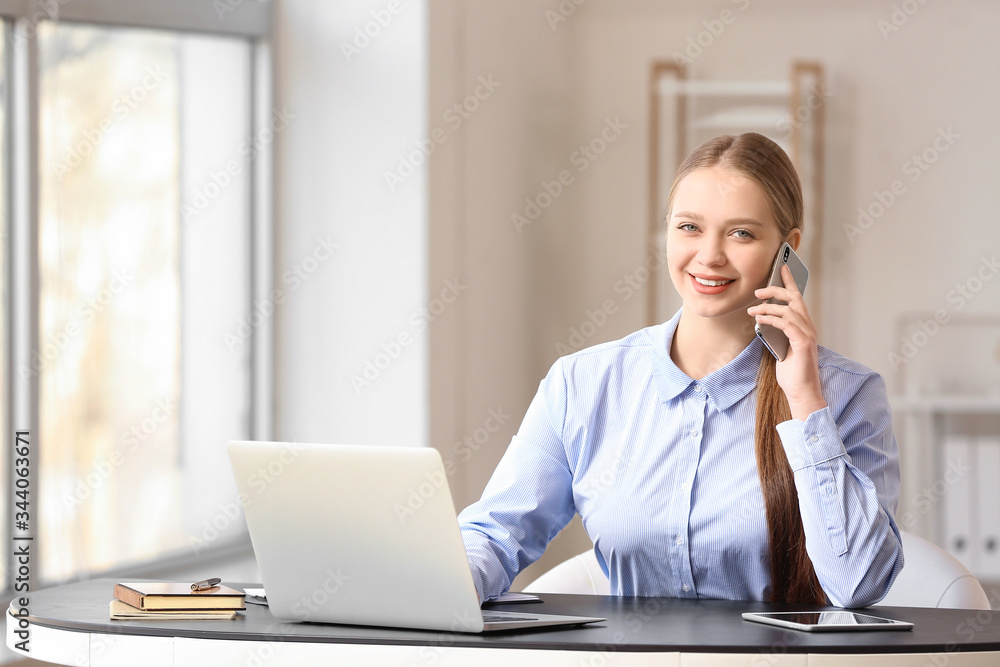 Portrait of young businesswoman talking by phone at table in office Portrait of young businesswoman talking by phone at table in office
