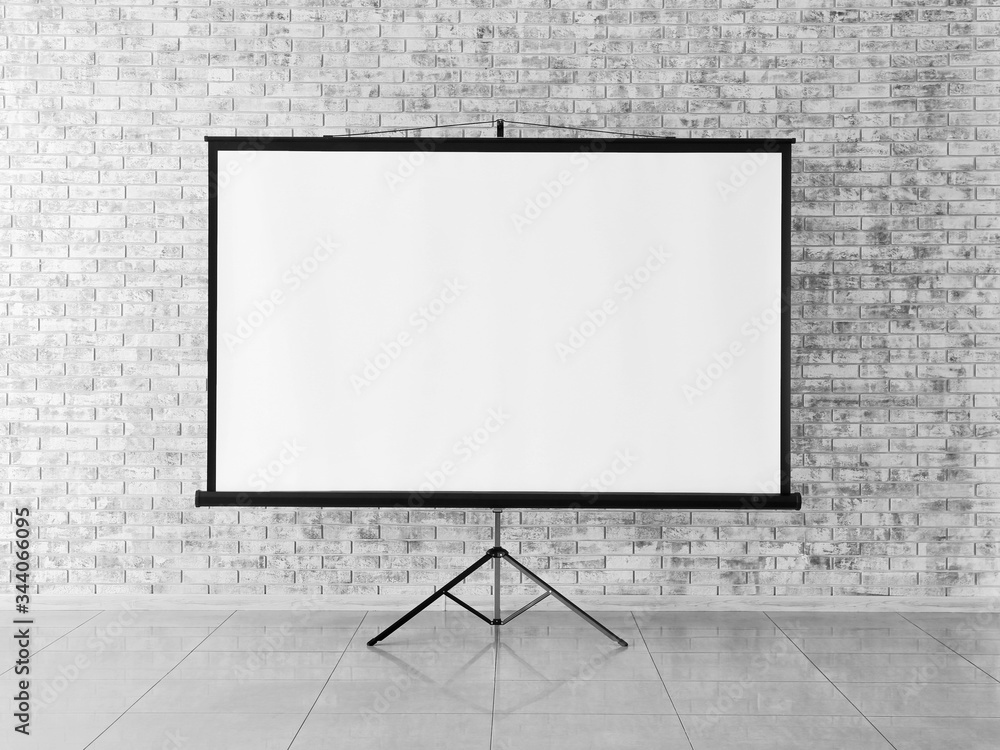© Pixel-Shot - Modern projector screen near brick wall indoors