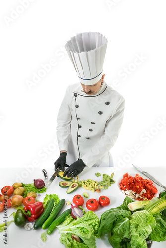 Chef cook cuts the avocado with a knife at the white table with a vegetables