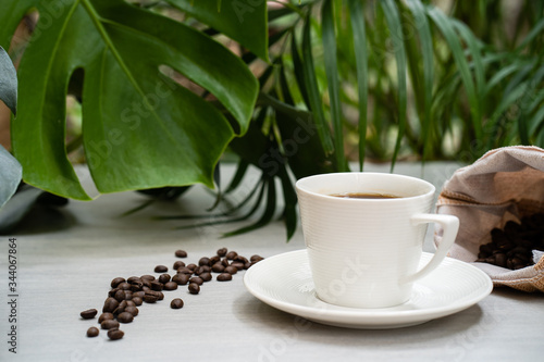 Cup coffee with sack roasted coffee bean against palm leaves background.