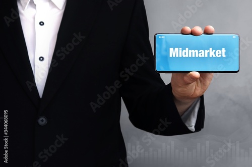 Midmarket. Businessman in a suit holds a smartphone at the camera. The term Midmarket is on the phone. Concept for business, finance, statistics, analysis, economy photo