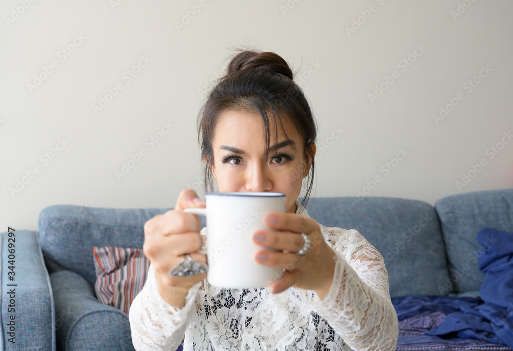 Beautiful woman holding coffee cup show to camera looking in room background.