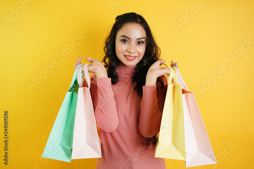 confident happy smiling teenage woman shopping. Portrait of customer woman hand holding shopping bag isolated over yellow background.