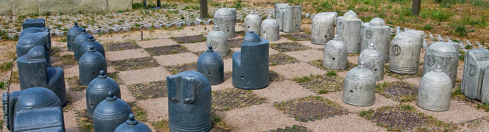 Stone chess pieces on the ground. Stylized chess Board with stone chess pieces outdoor in the park. Stone chess pieces on the ground. Stylized chess Board with stone chess pieces outdoor in the park.