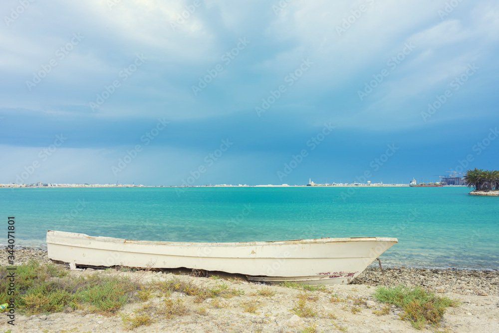 Wooden white boat parking on the sea sand beach over blue water and sky background, Bahrain.
