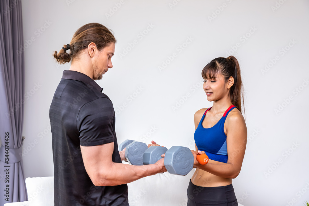 Attractive girl doing dumbbell weight exercises with personal trainer at home Attractive girl doing dumbbell weight exercises with personal trainer at home