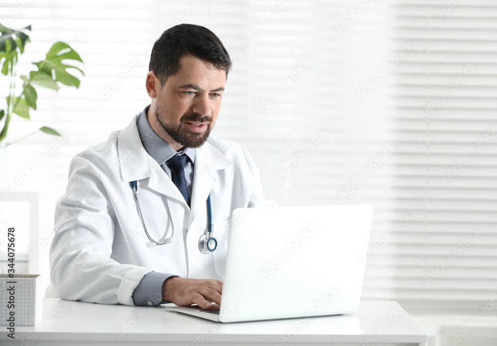 Male doctor working with laptop at table in office Male doctor working with laptop at table in office