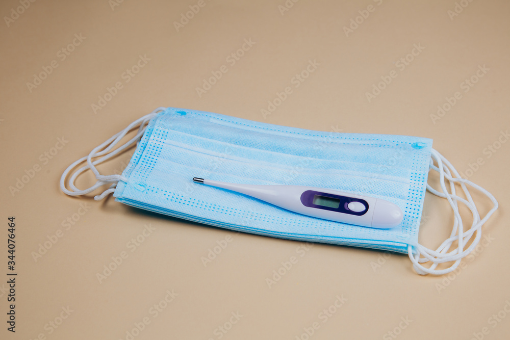Medical masks and digital thermometer on a beige background. Medical masks and digital thermometer on a beige background.