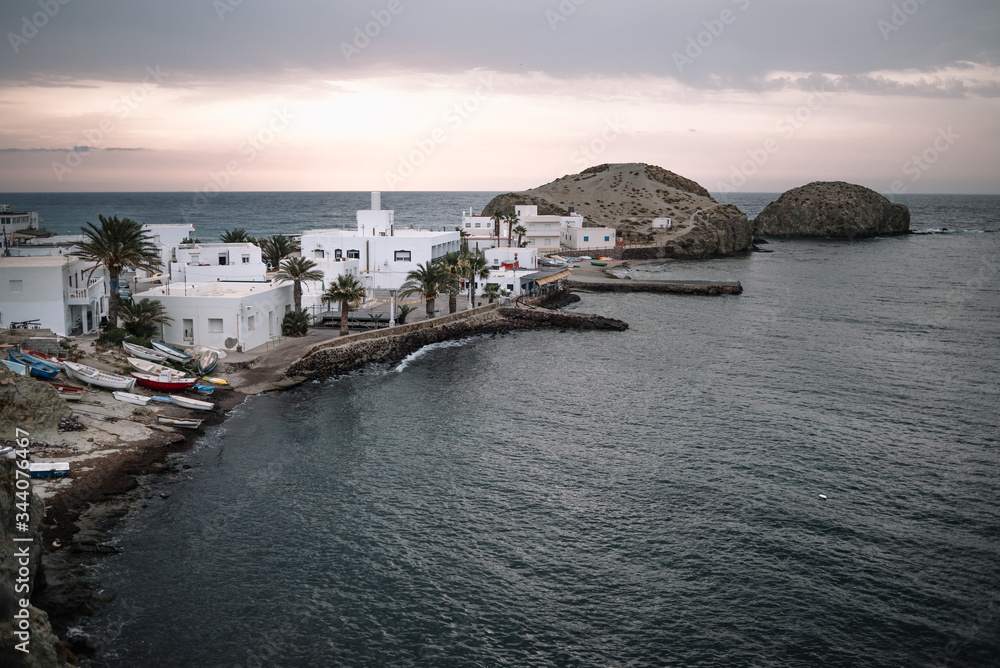 La Isleta del Moro, a small town by the sea at dawn with boats moored out of the water, typical white houses with undamaged land and palm trees.