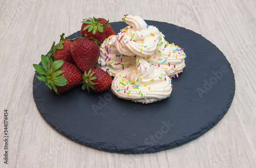 
meringues with strawberries on black plate and white background