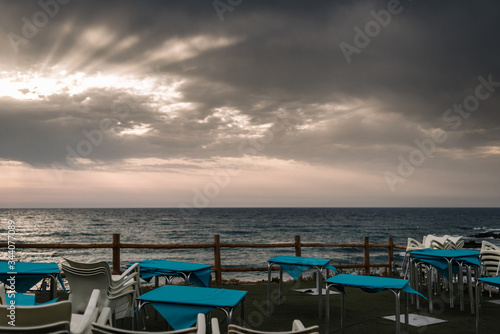 Empty restaurant terrace facing the sea on a cloudy day with sunrays in Almería, Spain. © Miguel