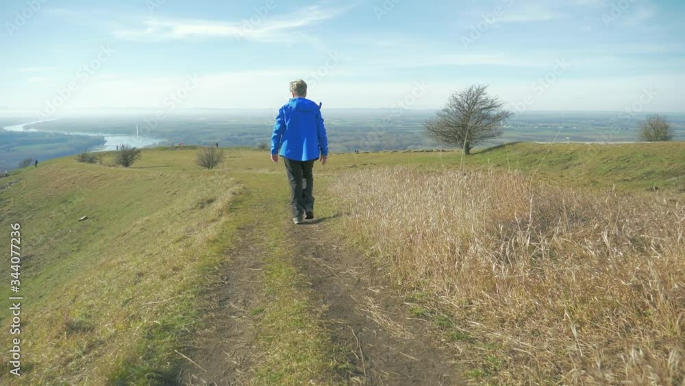 Hiker in Blue Coat Walking Downhill Towards Beautiful Vast Backdrop Hiker in Blue Coat Walking Downhill Towards Beautiful Vast Backdrop