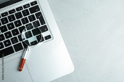 Magnifying glass and modern laptop on light grey table, space for text. Search concept photo