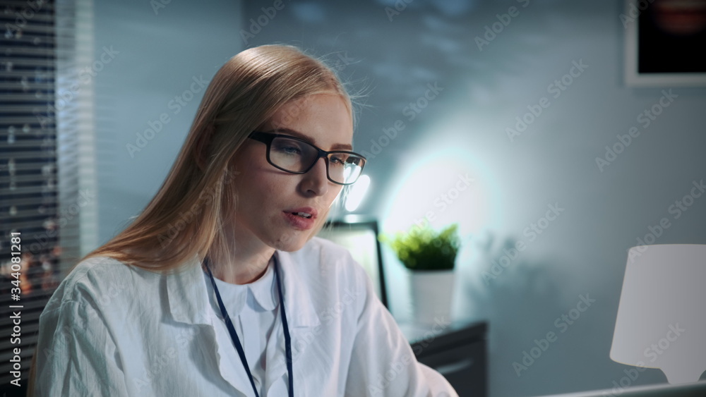 Close-up of female psychologist in eyeglasses and lab coat making video call with patient by computer and giving important advices in modern office Close-up of female psychologist in eyeglasses and lab coat making video call with patient by computer and giving important advices in modern office