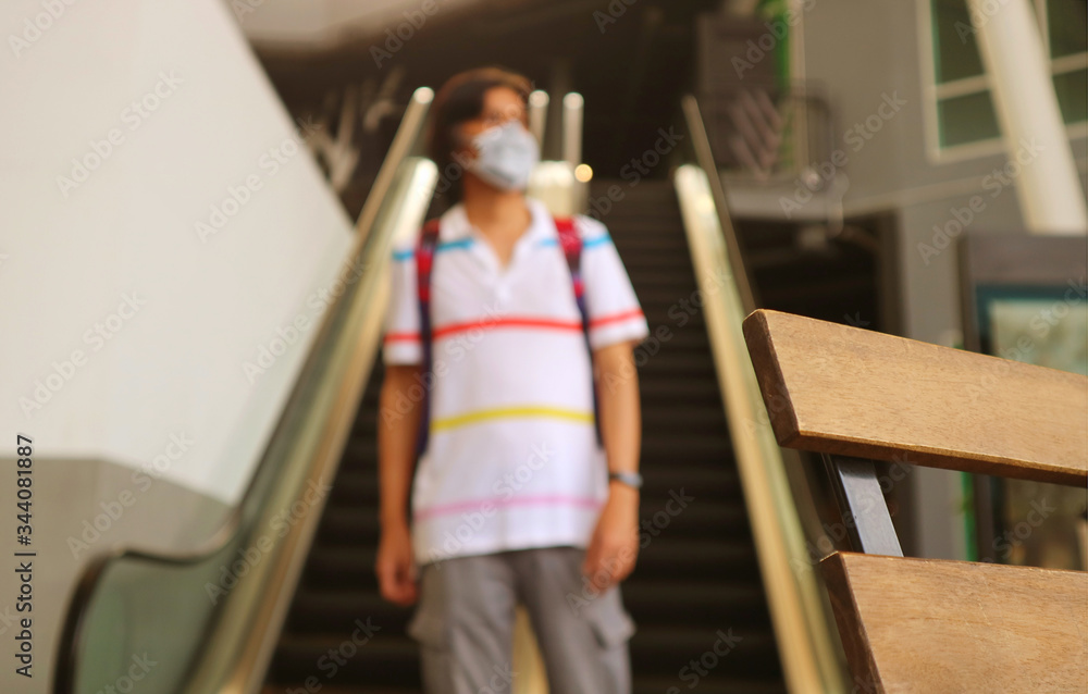 Closeup a wooden chair with blurry young man wearing face mask walking alone in a modern building